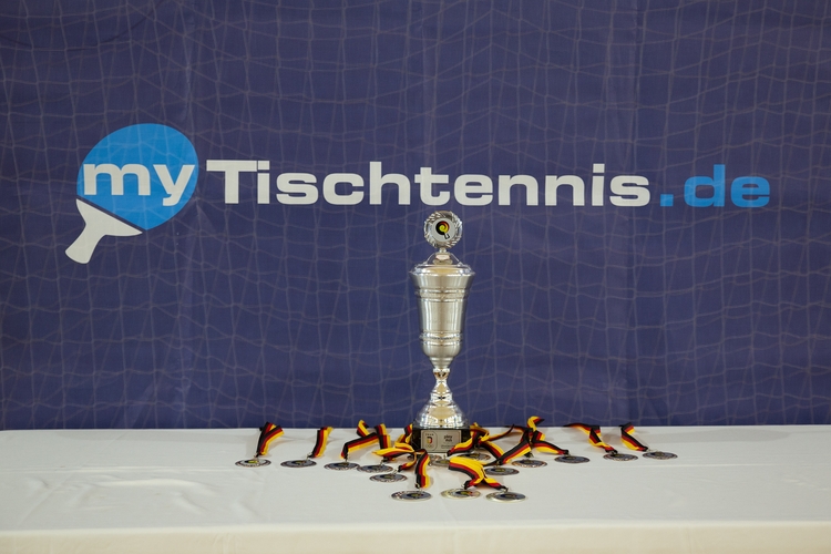 Der Pokal wurde schon vor dem ersten Aufschlag zur Schau gestellt. Unter dem myTischtennis-Banner waren zudem die Siegermedaillen ausgelegt. (©Fabig)
